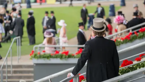 In the foreground a man in a top hat and suit overlooks a blurry Ascot racecourse.