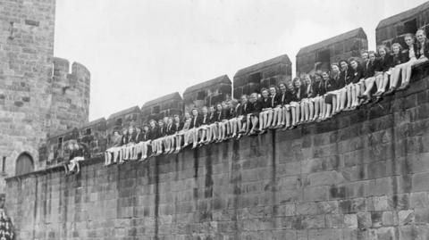 A row of girls sitting on a wall of Alnwick Castle 