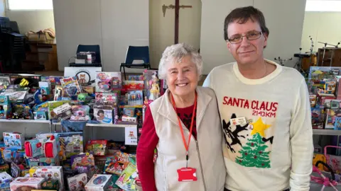 Joyce Whitt and Nick Clark stood in front of a table piled with toys