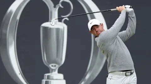 Rory McIlroy delivers an iron shot with the Open Championship logo behind him