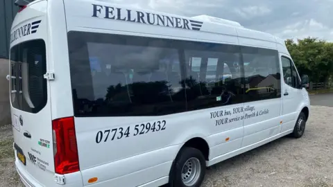 A white minibus pictured side-on with the words Fellrunner on the side, at the top. A mobile phone number and a corporate message runs along the side.