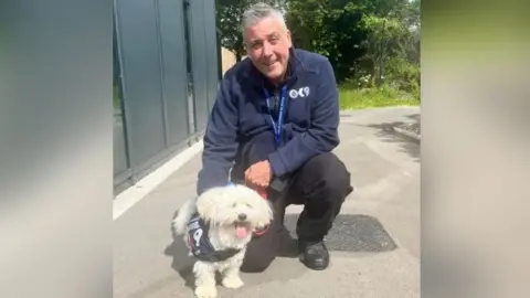 Bedfordshire Police A small fluffy white dog next to a man in a blue jacketkneeling beside it