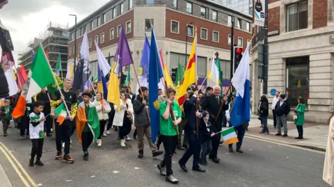 People walking in a parade hold Irish flags and the flags of Irish counties while walking through Leeds city centre.