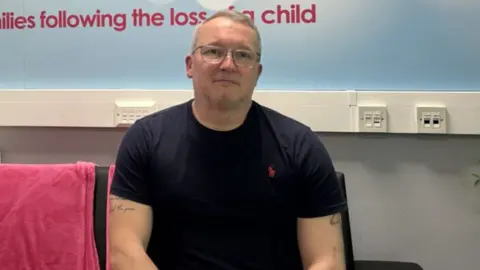 Rob sitting on a sofa next to a pink blanket.
