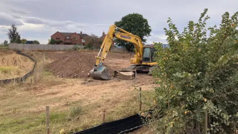 A digger is seen digging into a mound of clay and dirt.
