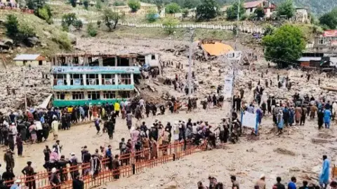 Afghan National Disaster Management Authority Scores of people standing outdoors as floods ravaged the town of Parun in Afghanistan's Nuristan province