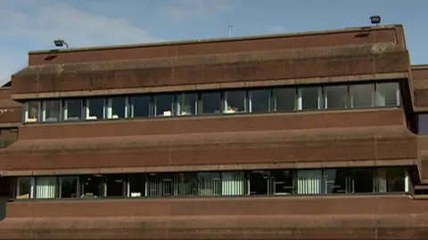 An image of a red brick building which is two storey. There are windows where you can see blinds and the inside of office spaces. 