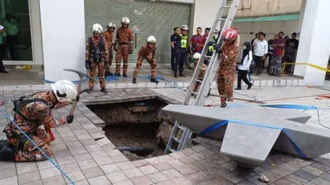 Malaysian rescuers try to enter a sinkhole in Kuala Lumpur to rescue a woman who was suddenly swallowed by the pavement.