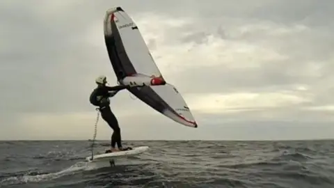 Wing foiler in the sea moving away from the camera