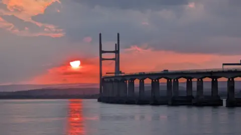 A bridge with a bright sunrise behind it