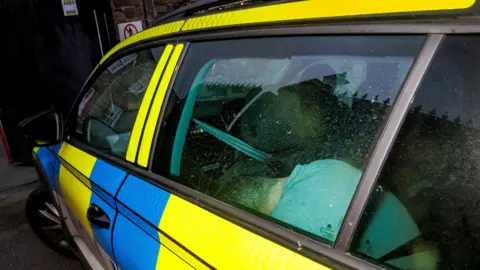 Photo taken of Connor Pollock through the back window of a yellow and blue PSNI car with his head down