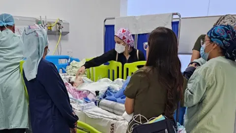 Family handout Sienna-Rose, in a hospital bed, surrounded by medical staff.