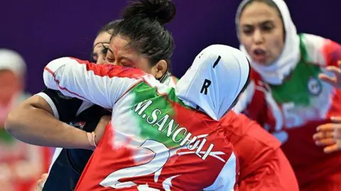 Getty Images Iran's team competes against Nepal during the Hangzhou 2022 Asian Games in 2023. Women are competing, two wearing head coverings, and two players are blocking another woman.