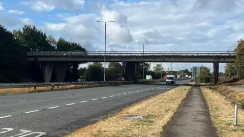 National Highways Cars travelling on a dual-carriageway with a bridge in the background.