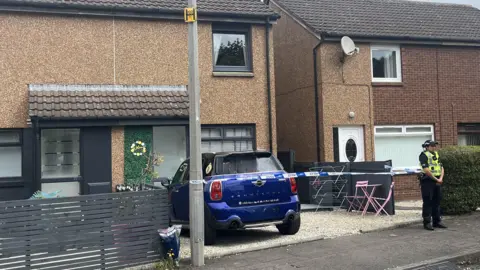 a female police officer stands outside a cordoned-off house