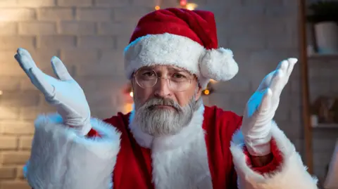 Stock image of a man dressed as Santa Claus with his arms held up in a questioning pose