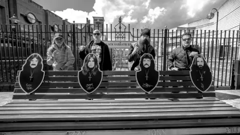 Pantera Four members of Pantera stand behind a bench which has images of the four members of Black Sabbath