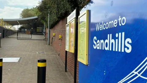 A blue sign with 'Welcome to Sandhills' in white text at Sandhills station