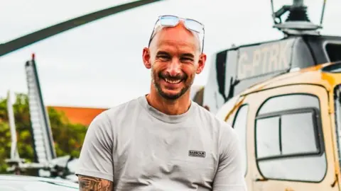 A man with a grey t shirt and no hair with sunglasses on his head