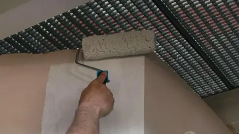 Stock image of a man using a paint roller with white paint on a wall