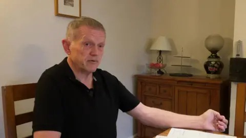 Richard Barker sitting at his dining room table looking over paperwork to do with his investment in Arndale House in Liverpool. 