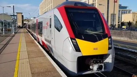 A Greater Anglia train parked next to the platform in Cambridge. The train is grey with red and yellow panels.