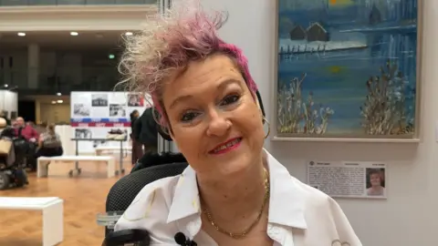 Woman smiling, head tilted and a painting on a wall 