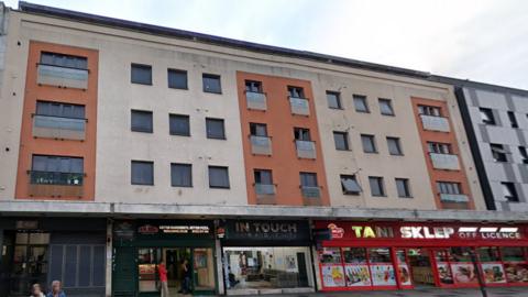 A building in High Street with a row of shops at its ground floor and then three floors of flats, with 12 windows across 