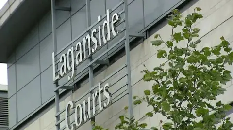 Image of a sign saying Laganside Court on a light coloured building surrounded by trees