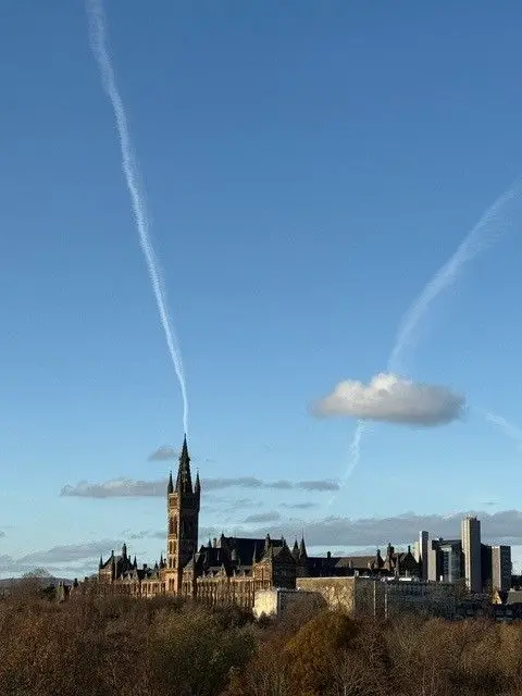 Shanti Nelson The Glasgow University main building with its bell tower. There are a couple of clouds but the sky is blue and there are trees below the building.