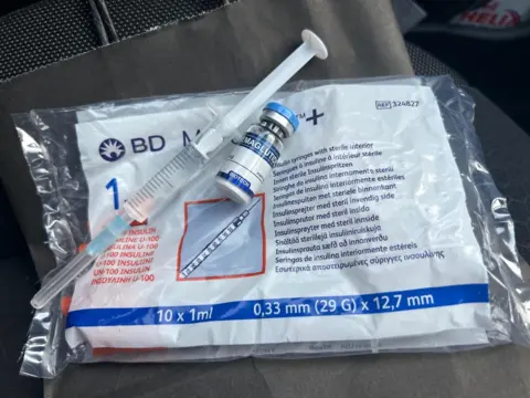 A syringe filled with liquid, vial marked "semaglutide" and bag of insulin syringes