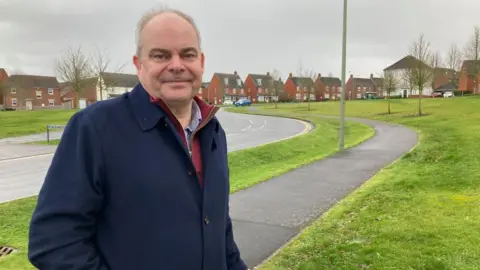 A man in a blue coat is standing next to a road on a new build housing estate.