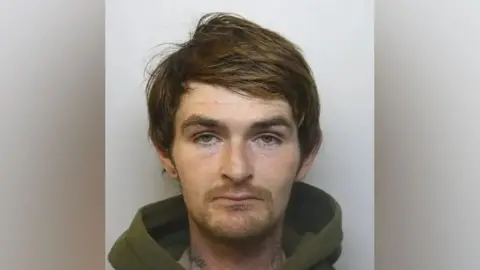 Cory Farrar's mugshot. He is wearing green hoodie and has a tattoo on his neck.