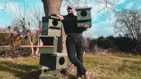 BETH MCRUDDEN Will is leaning on a stack of wooden bird boxes.