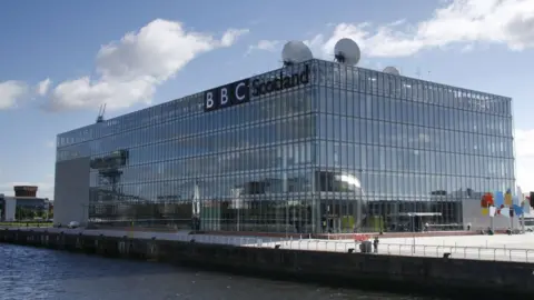A large glass box building with windows on all sides and satellite dishes on top