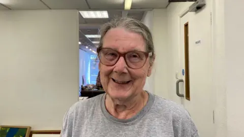 A woman with glasses and a grey T-shirt. She smiles at the camera.