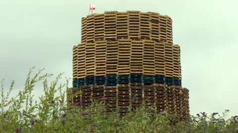 The bonfire that's built with red, white and blue pallets. Below is some shrubbery.