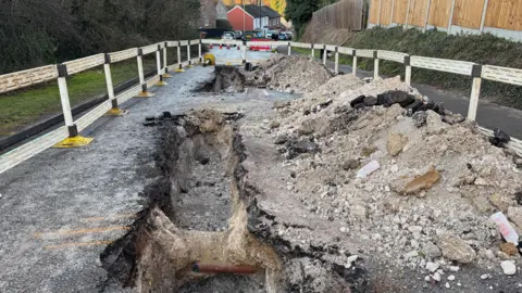 Janine Machin/BBC A road that has been dug up by engineers to fix a gas leak revealing a large hole, which has been cordoned off.