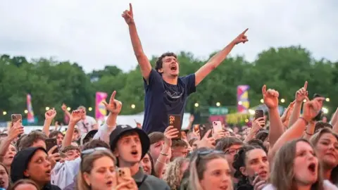 An excited crowd of people at the Big Weekend - with their hands in the air and some people on each other's shoulders. 