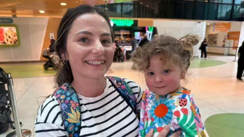 A woman carrying a toddler, both smiling at camera