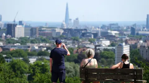 Three people overlook London's skyline on a sunny day.