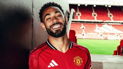 A smiling Matheus Cunha wearing a Manchester United shirt