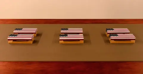 Jack Elliot Edwards Small objects featuring coffins draped in the American flag from Tanoa Sasraku's Morale Patch installation at the Institute of Contemporary Arts, London