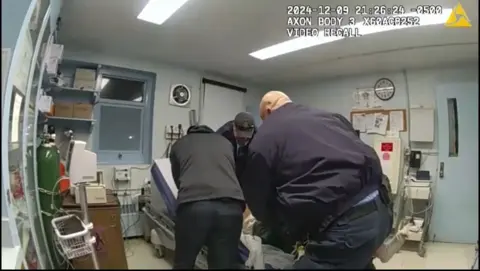 New York State Attorney General's Office A group of men huddled around an examination table in a medical office, it is apparent that someone, barely visible, is on the table itself