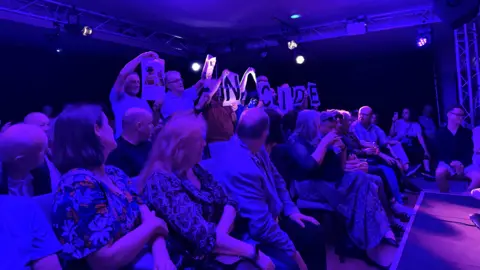 PA Media Protesters holding up signs in an audience