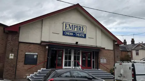 Adam Bennett/BBC The Empire Theatre in Halstead, pictured from the street. The building is white with a pitched roof and a sign that says Empire Cinema Theatre