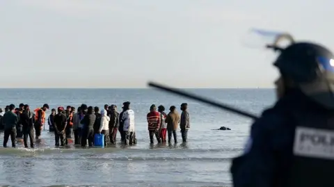 People thought to be migrants wade through the sea to board a small boat leaving the beach at Gravelines, France, in an attempt to reach the UK by crossing the English Channel.