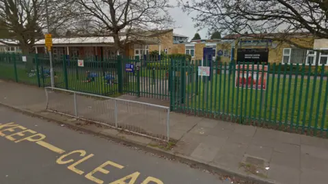 Google The entrance of an infant school with railings, pavement and road with a "keep clear" painted on the road outside.