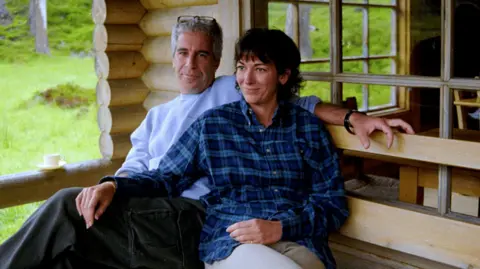 Maxwell (right) pictured with Epstein outside a wooden cabin. They are in causal clothes and she has her hand on his knee. This is one of the images released by the US Department of Justice