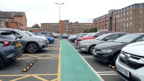 BBC A green path down the middle of the shot, with cars either side. In the background are office buildings.